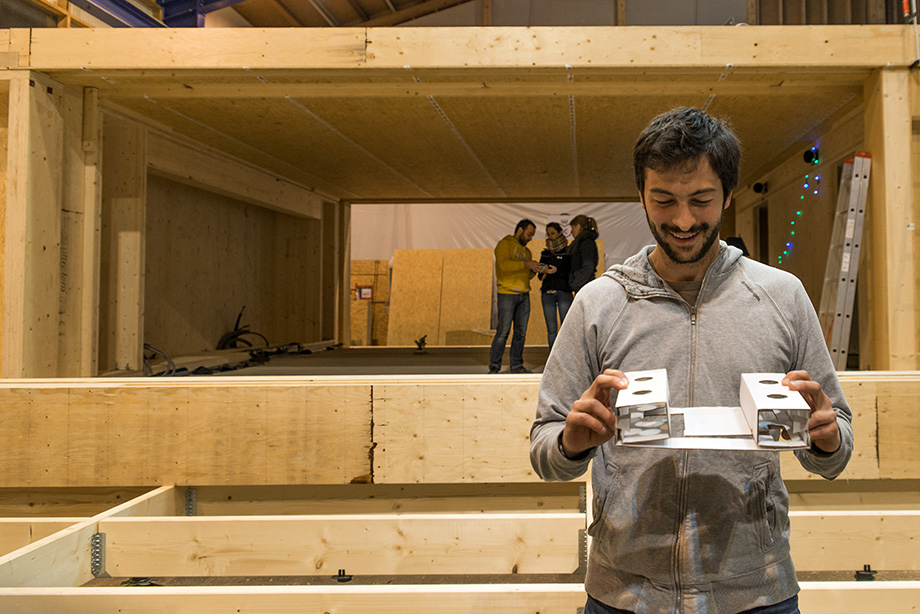 Johannes holding up a small model of the house. In the background, the real house