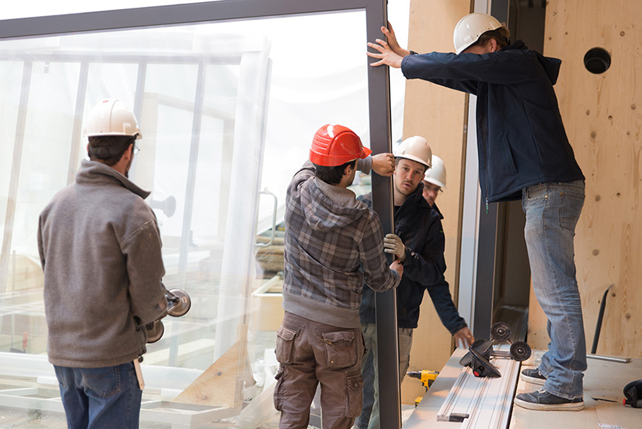 Five decathletes lifting a single window into its sliding frame