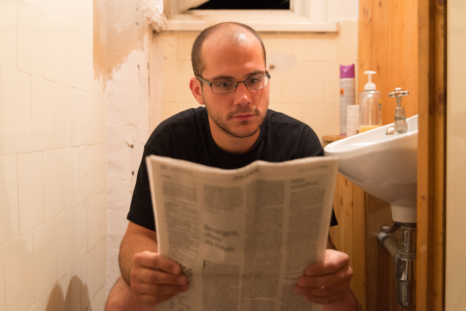 Rainer is sitting on the toilet and reading the newspaper