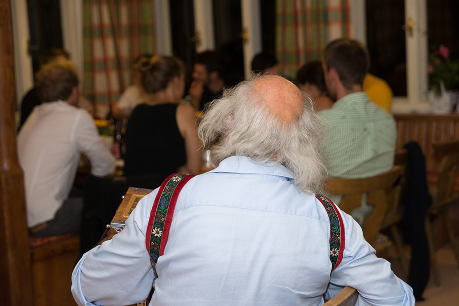 An old, greyhaired man seen from behind. In the background are decathletes.