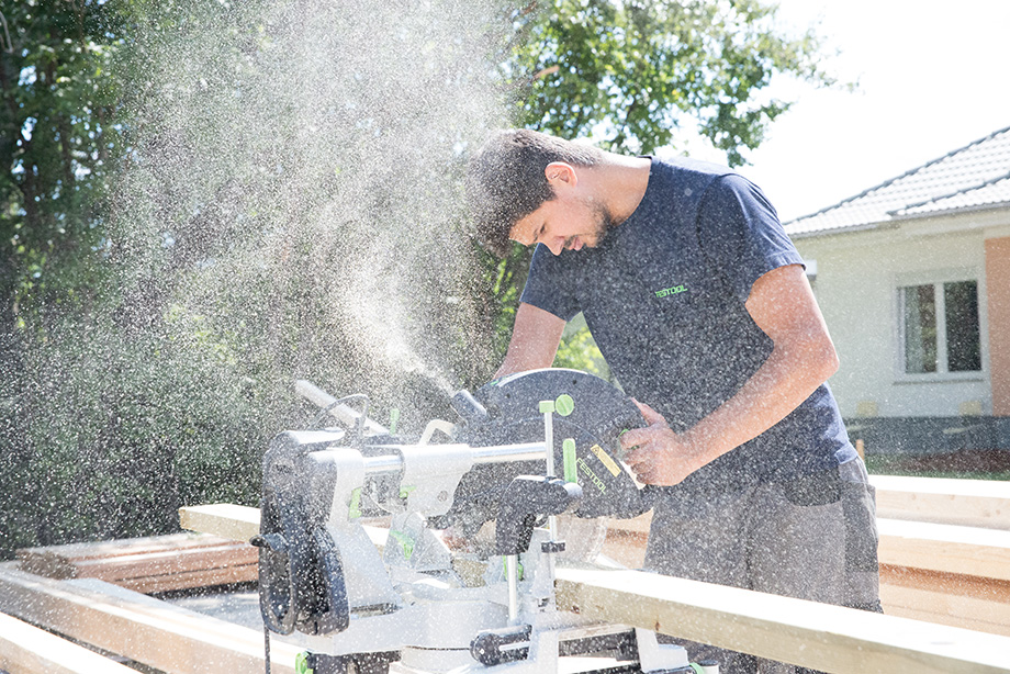 Decathlete Adrian is cutting a piece of construction wood. There's saw dust in the air.