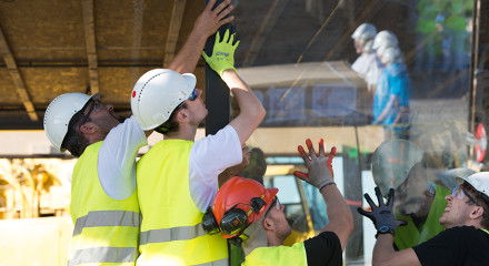 A group of decathletes are lifting a window into place.